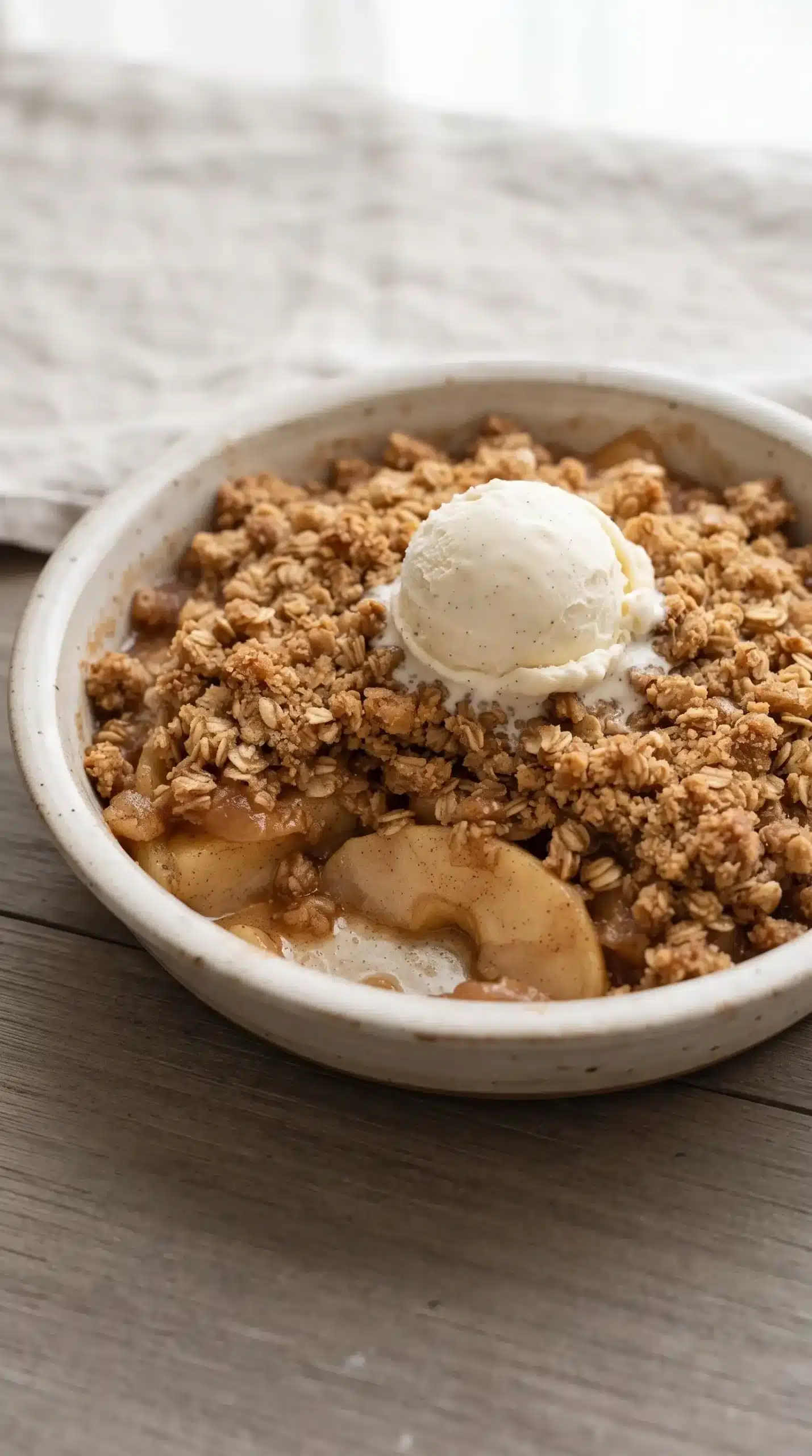 Warm apple crisp with golden oat topping and vanilla ice cream in a dish
