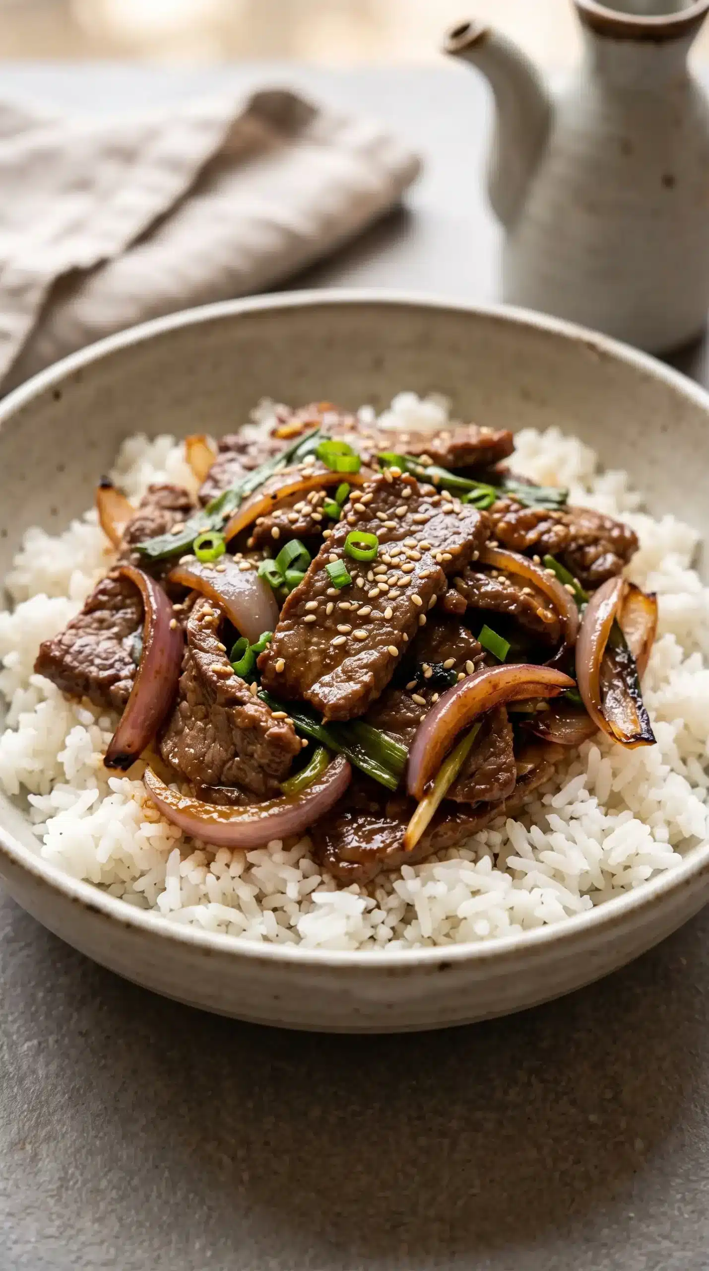 Beef onion stir fry with glossy sauce, rice, green onions, and sesame seeds