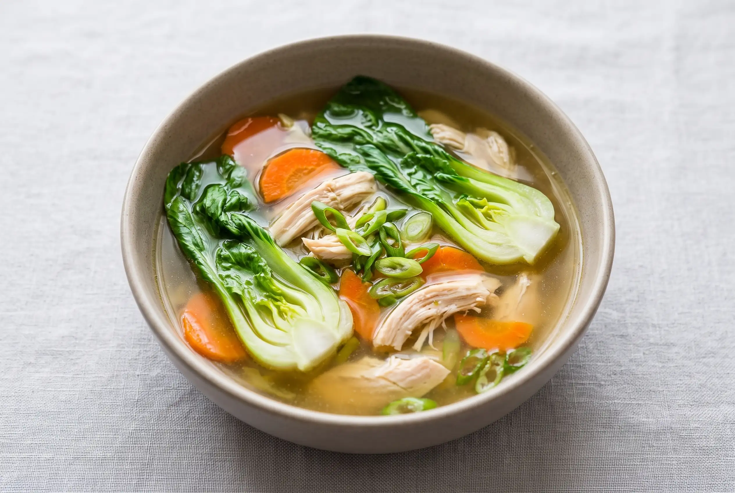 Bowl of bok choy chicken soup with garlic ginger broth, chicken, vegetables, and green onions