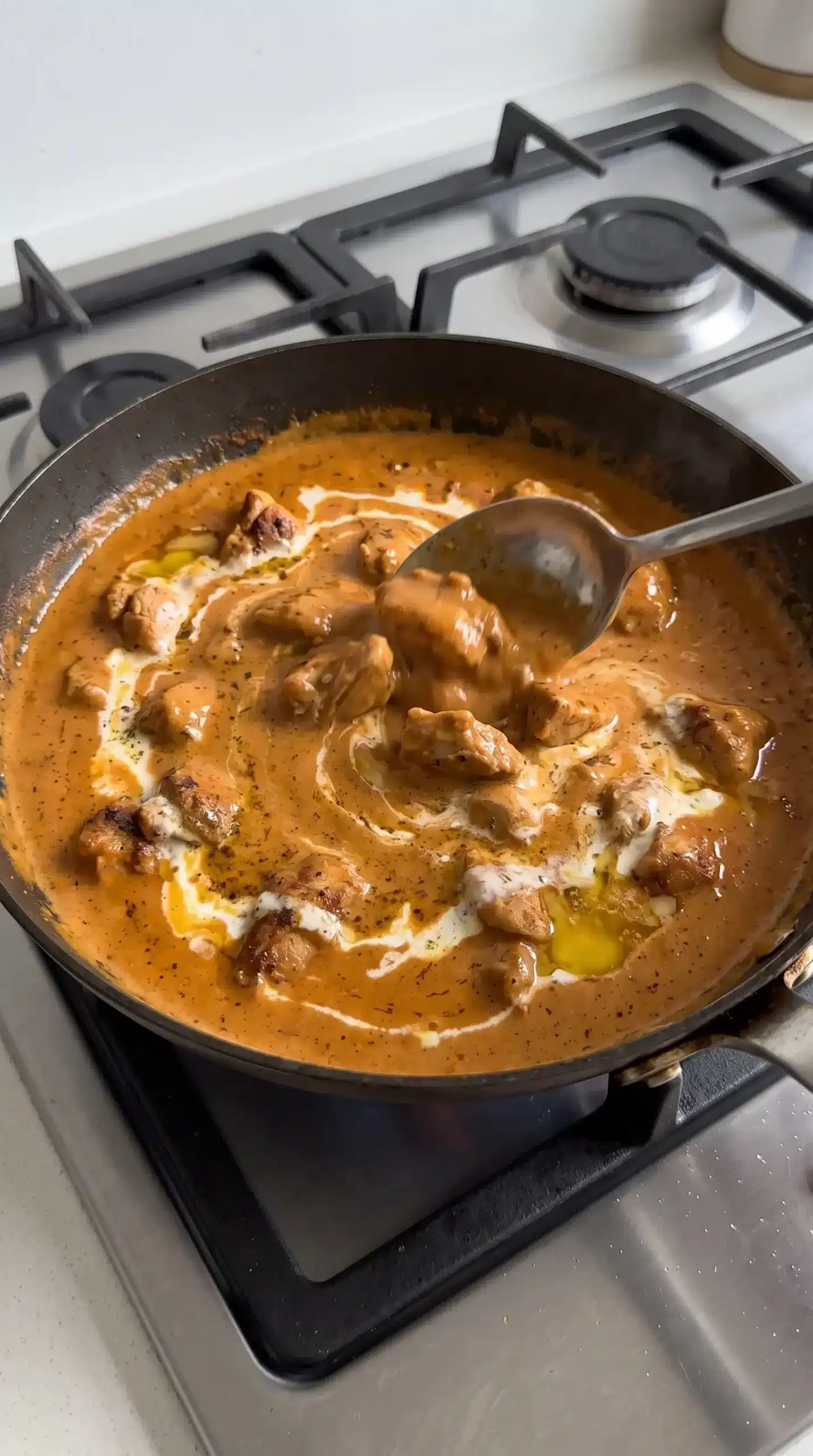 Chicken pieces simmering in a skillet with smooth tomato cream sauce for butter chicken