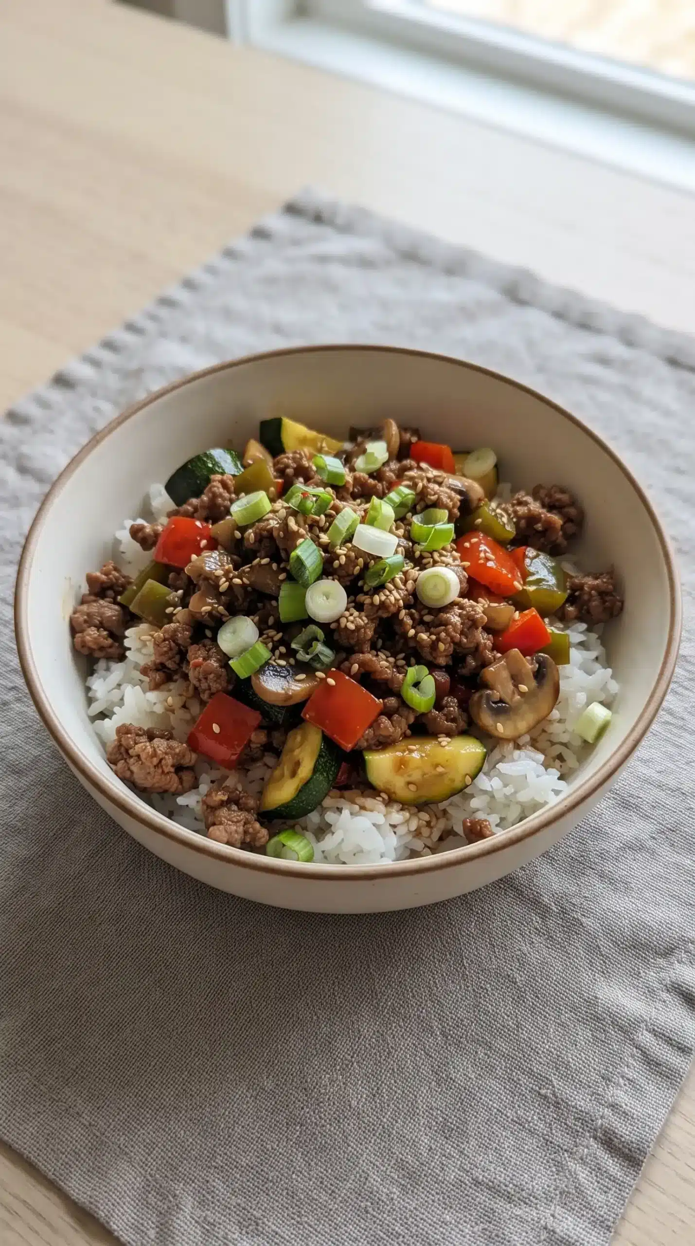 Finished ground beef stir fry bowl with rice, vegetables, sesame seeds, and green onions