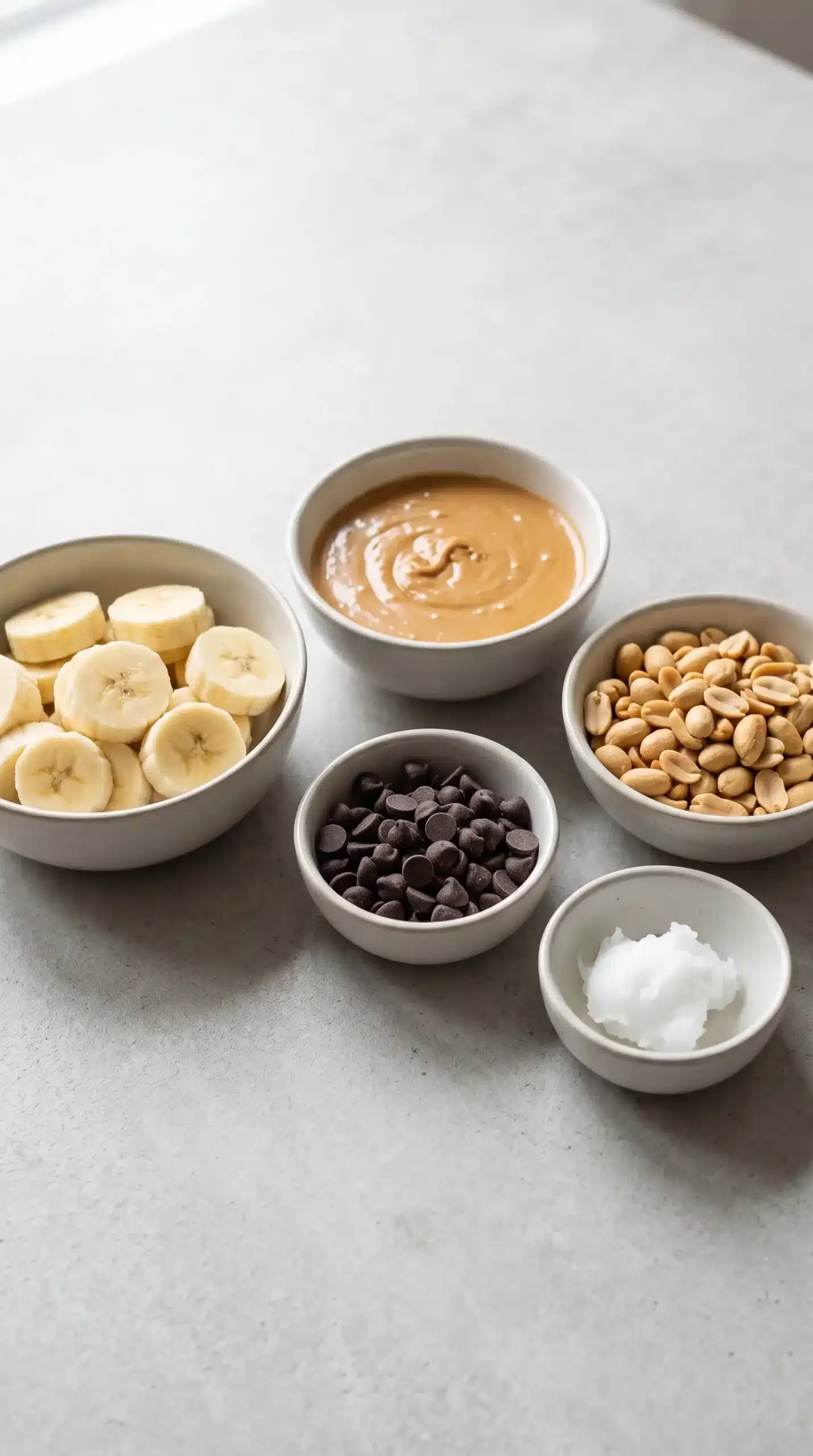 Ingredients for frozen banana snickers with banana slices, peanut butter, dark chocolate, peanuts, and coconut oil