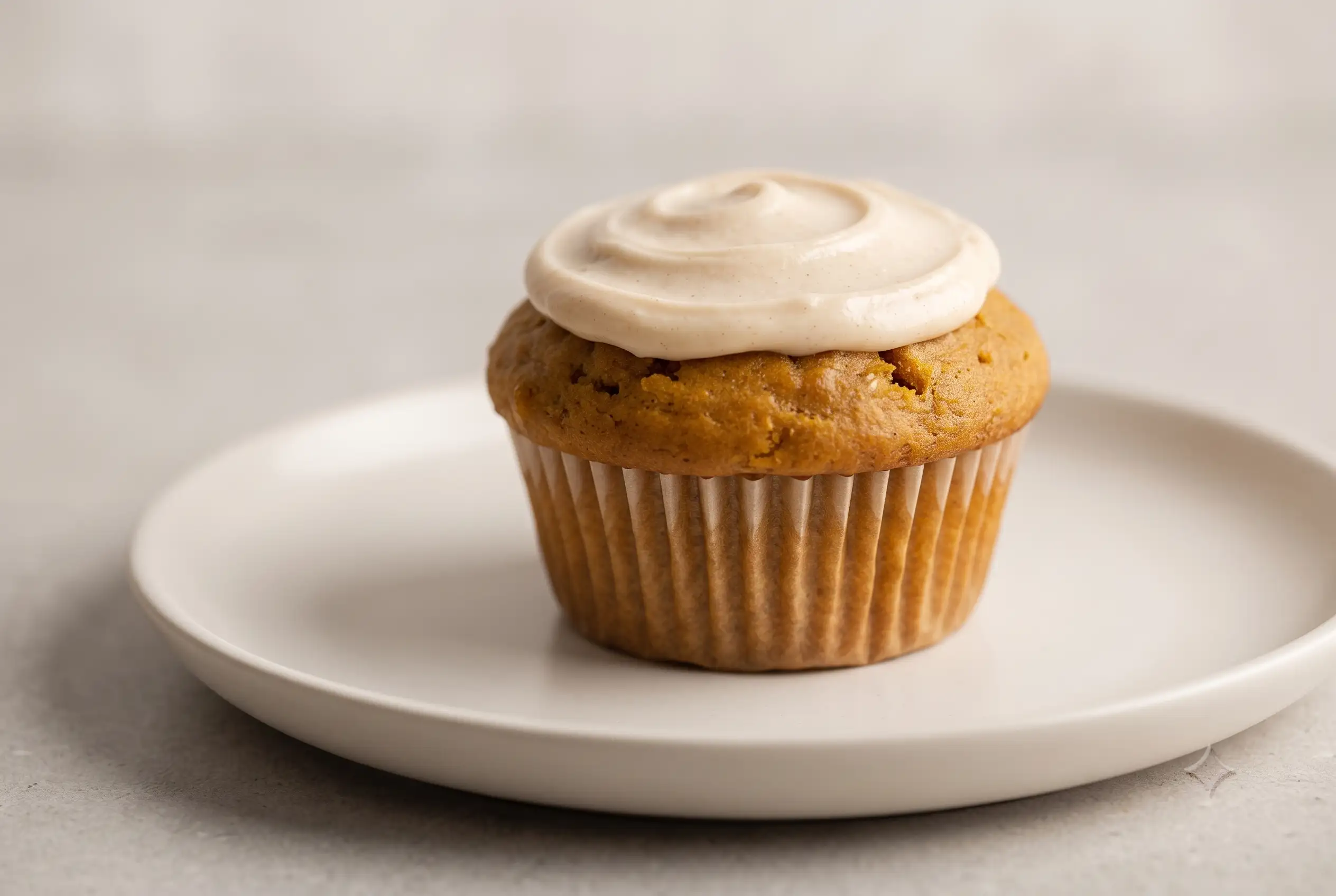 Keto pumpkin muffin with a golden top and low-carb cream cheese topping on a ceramic plate