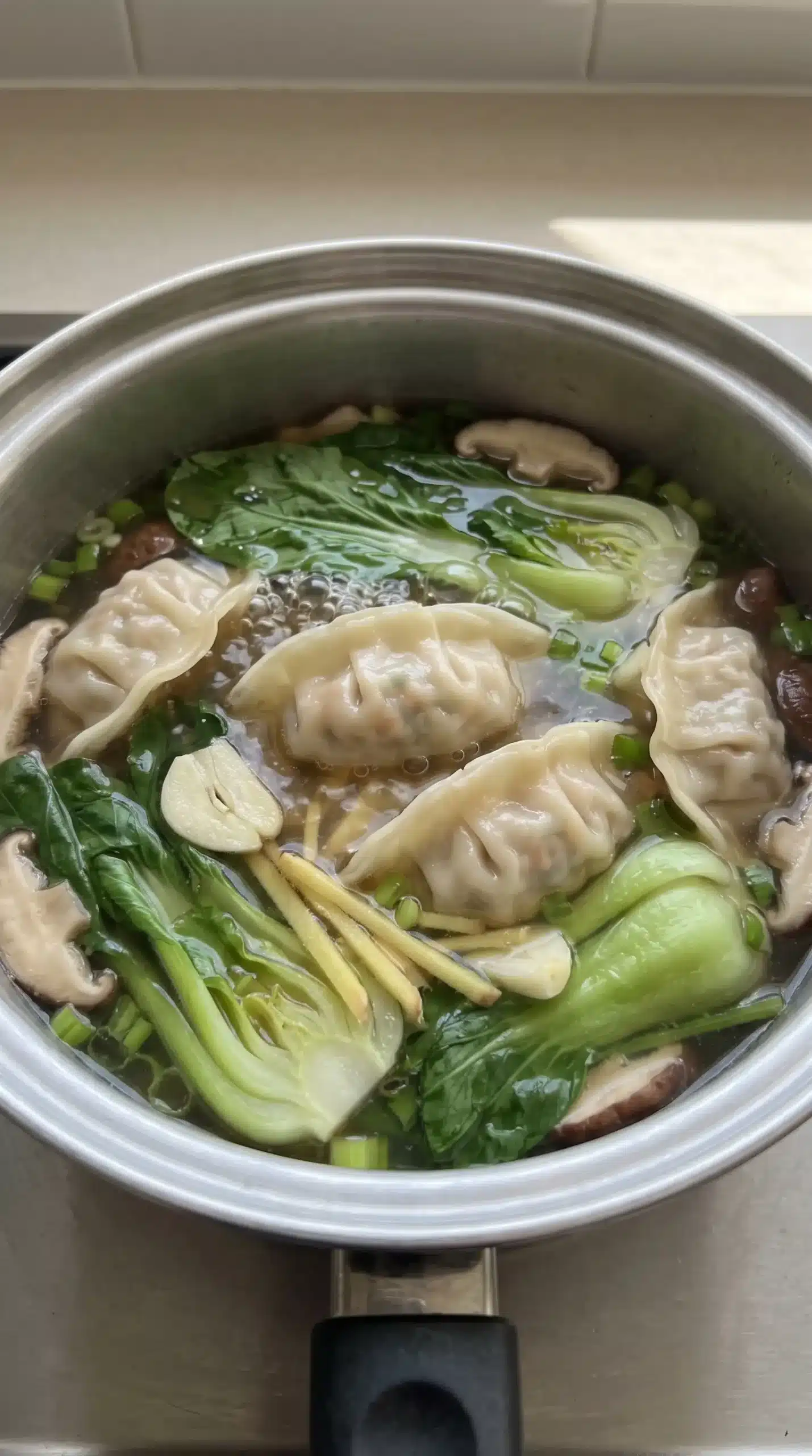 Potstickers simmering gently in seasoned broth with greens during soup preparation