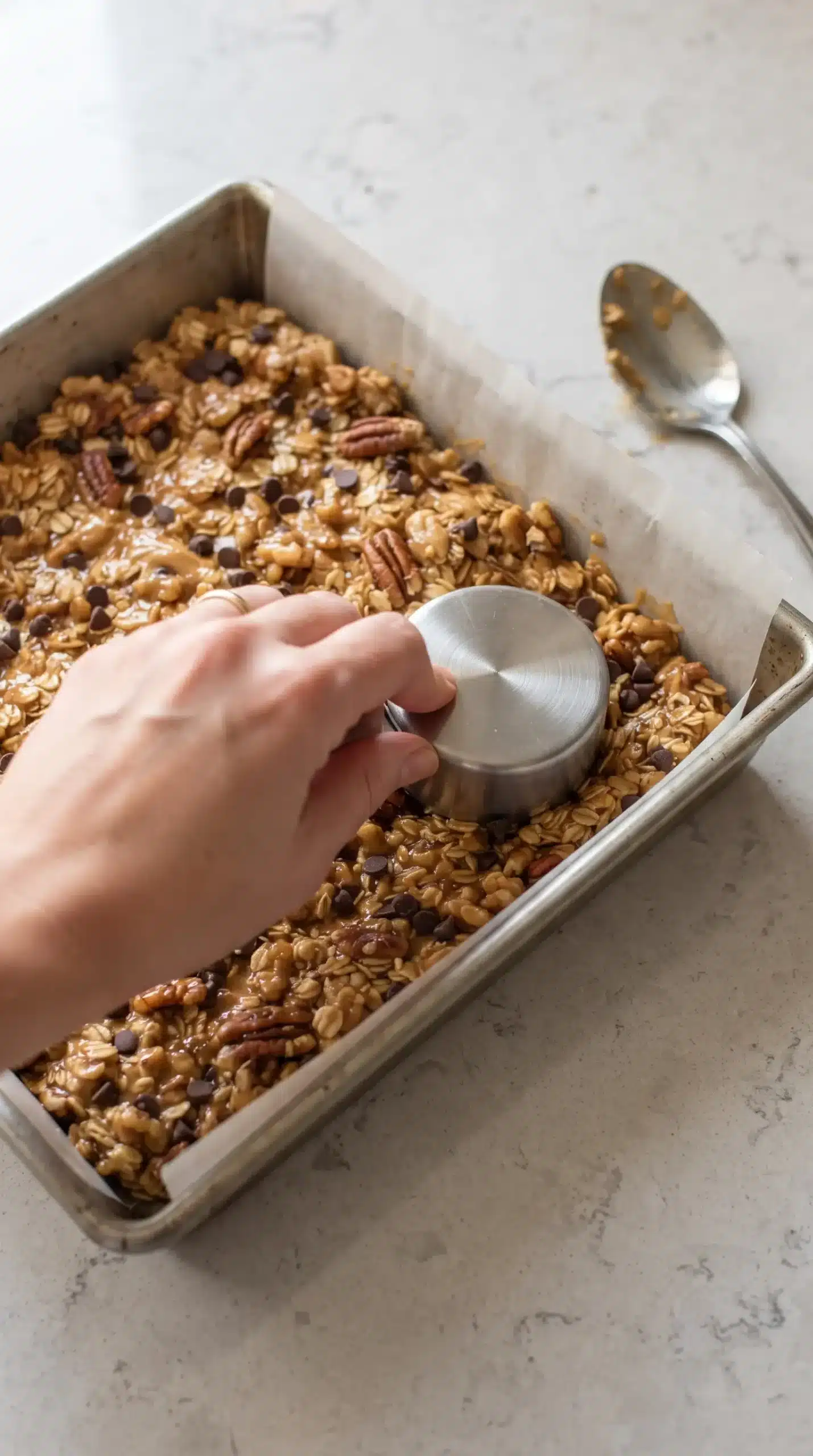 Granola bar mixture pressed firmly into a parchment-lined square baking pan