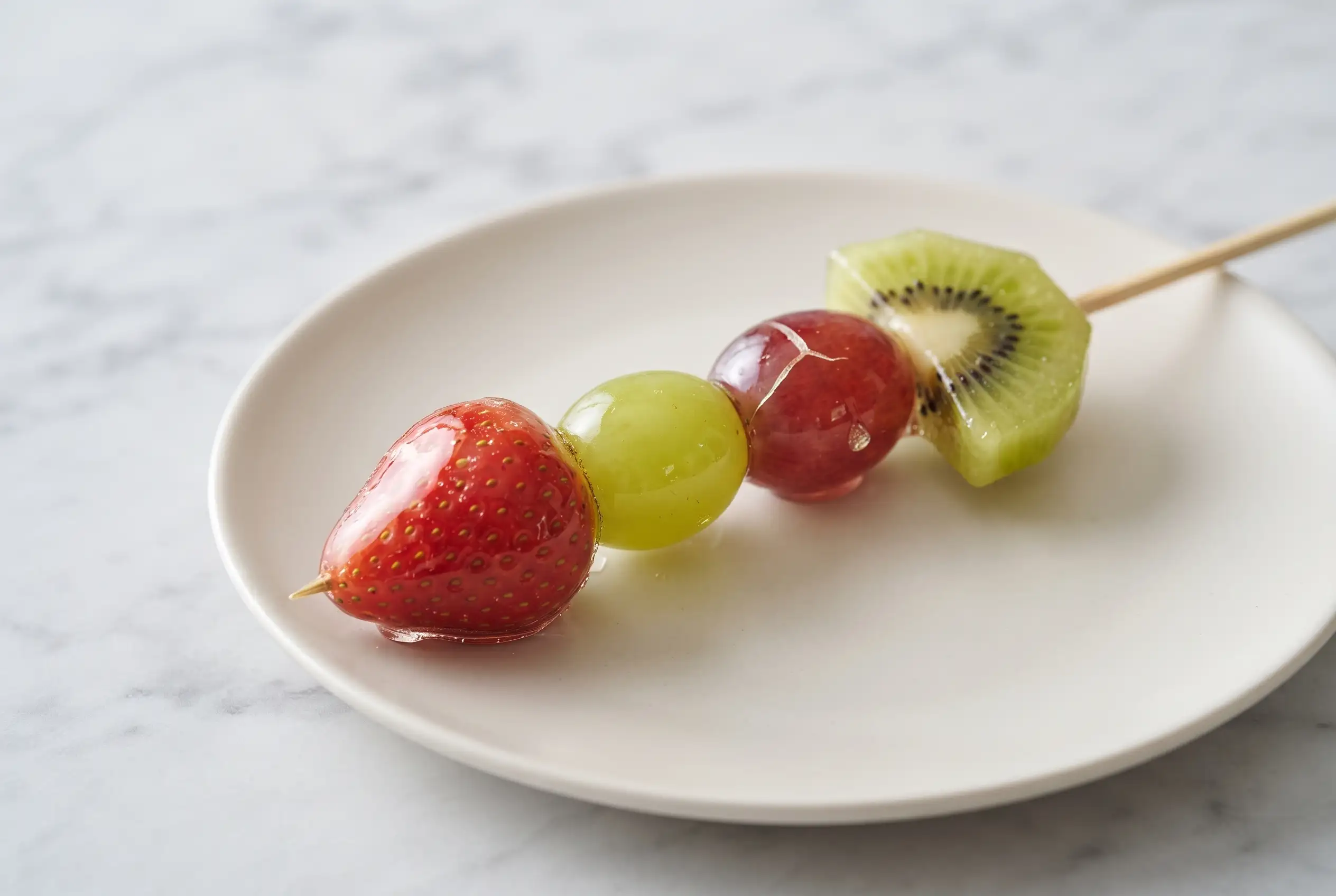Tanghulu recipe skewer with strawberries, grapes, and kiwi coated in a clear crunchy sugar shell